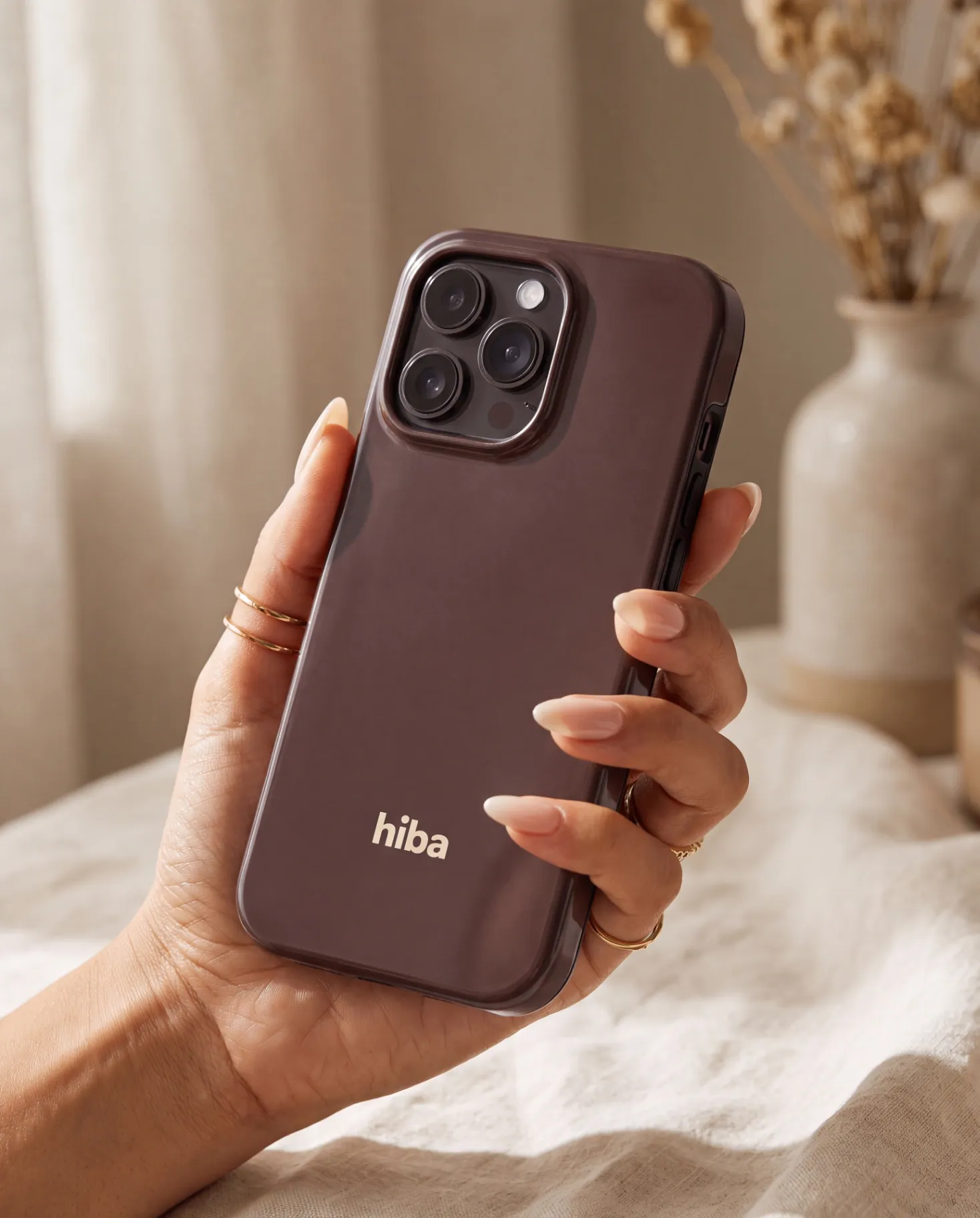 Hand with delicate gold rings holding the glossy Cocoa HIBA case